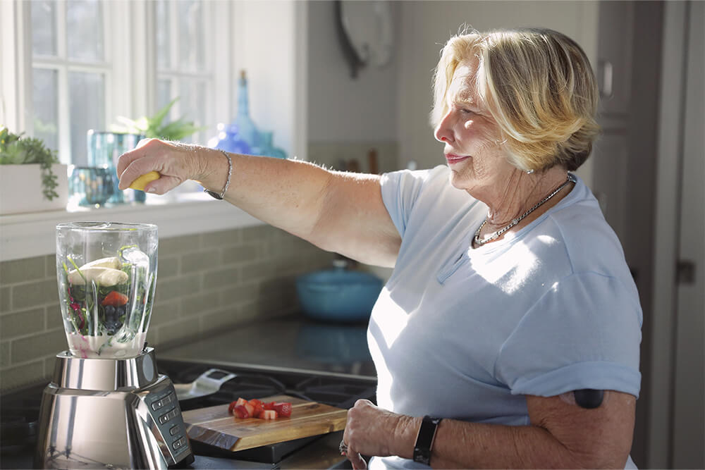 Kvinne lager en smoothie mens hun bruker en enhet for kontinuerlig glukosemonitorering.