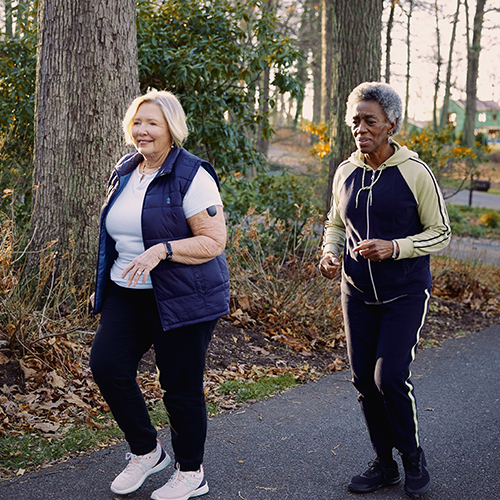 To kvinner med Eversense CGM-enheter som går utendørs.