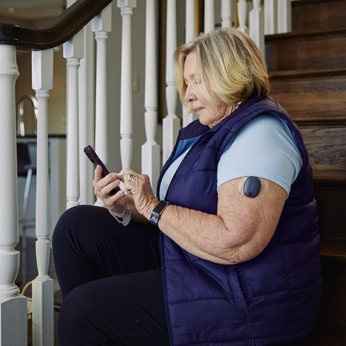 Kvinne sitter på trappen mens hun bruker Eversense CGM-appen med sin implanterbare CGM.